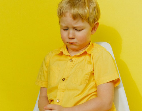 Sad child sitting on a white chair.