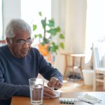 A man in a blue sweater sitting at a table with medications.