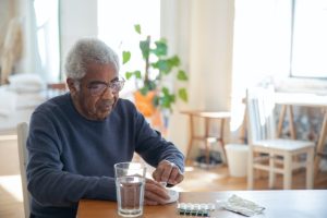 A man in a blue sweater sitting at a table with medications.
