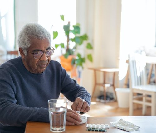 A man in a blue sweater sitting at a table with medications.